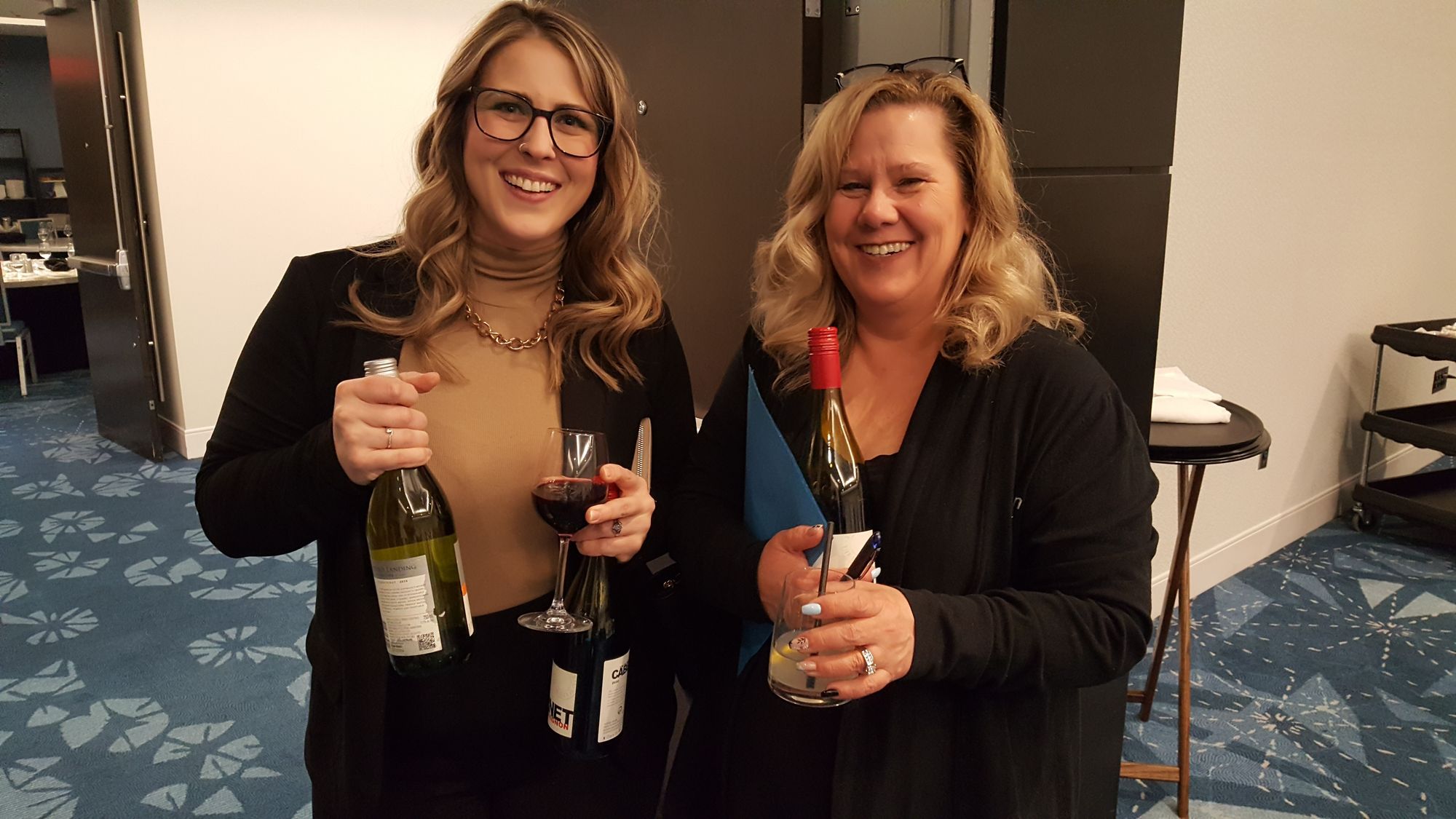 Two female friends smiling and holding wine.