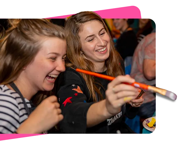 Two women laughing with a paintbrush 