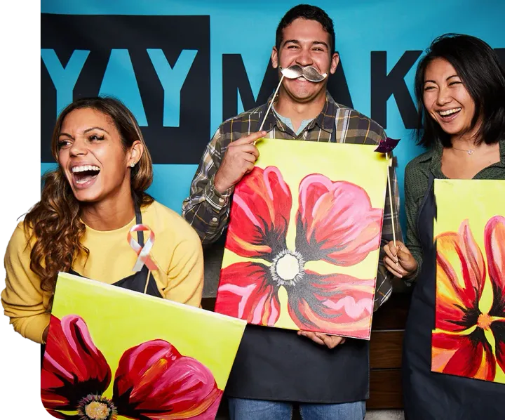 Three friends laughing with paintings at Paint Nite fundraiser