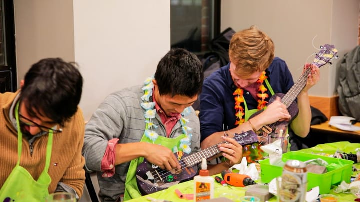 Three guys playing hand painted ukuleles in Paint Night aprons and leis
